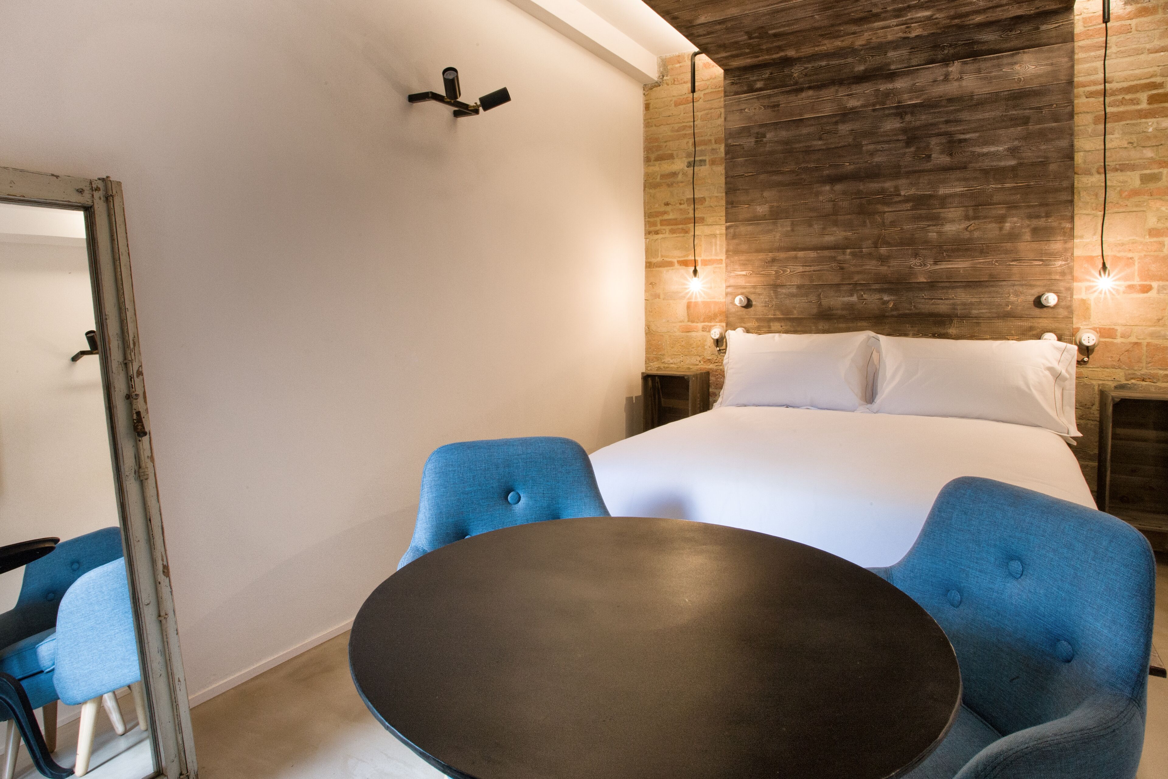 Habitación de hotel con una cama grande, dos sillas azules, una mesa redonda y una pared decorativa de madera.