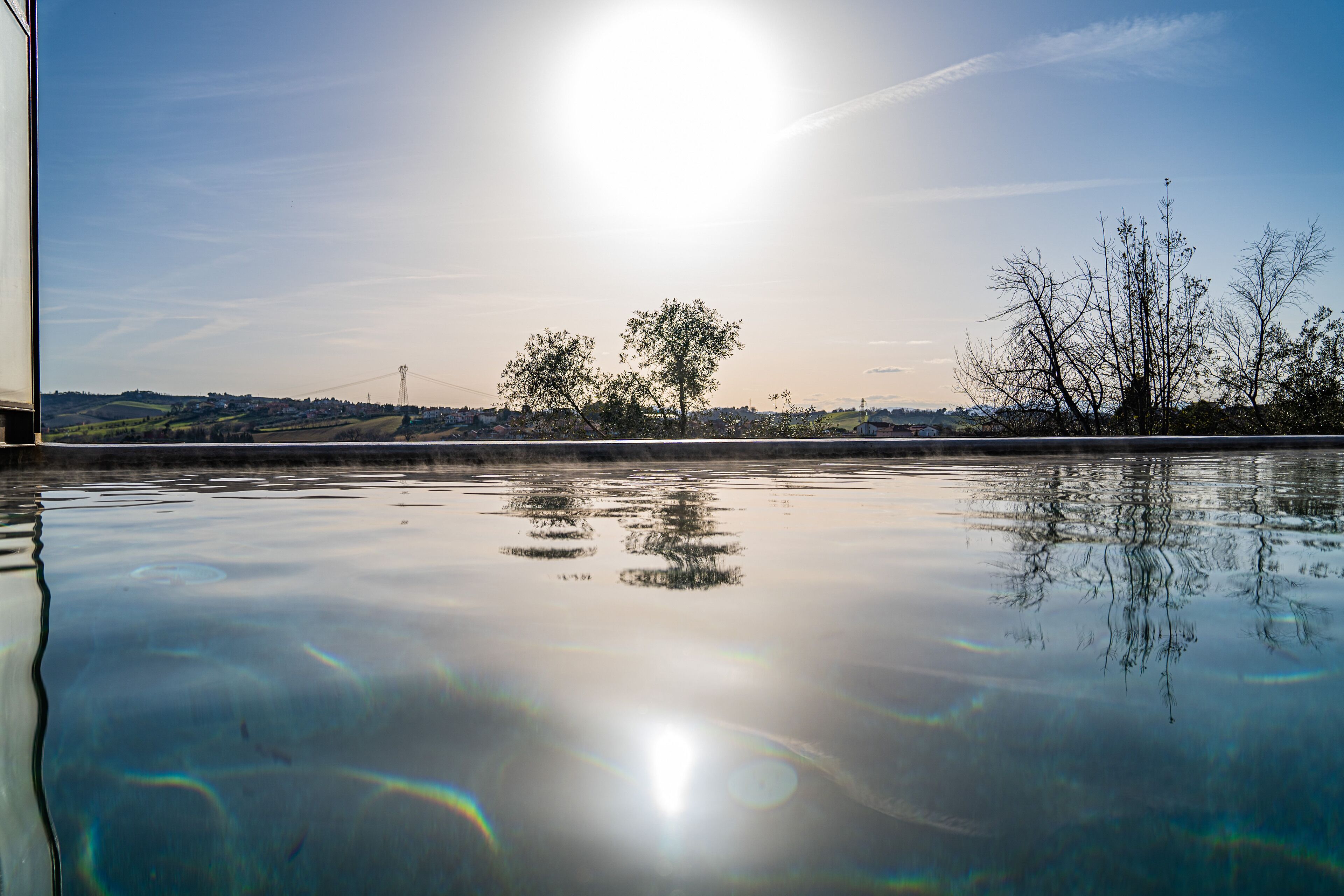 A calm body of water reflecting the sky and trees, with a distant view of a bridge and buildings.