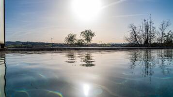 A calm body of water reflecting the sky and trees, with a distant view of a bridge and buildings.