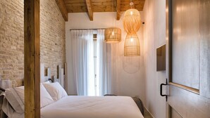 Un dormitorio con una cama grande, vigas de madera, una pared de ladrillo y dos lámparas colgantes.