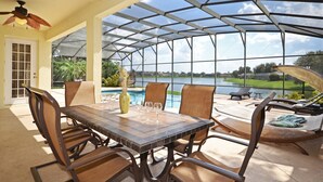 A covered patio with a table and chairs, a pool, and a view of a lake.
