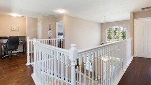 A spacious room with a wooden floor, a white railing, and a desk with a computer.