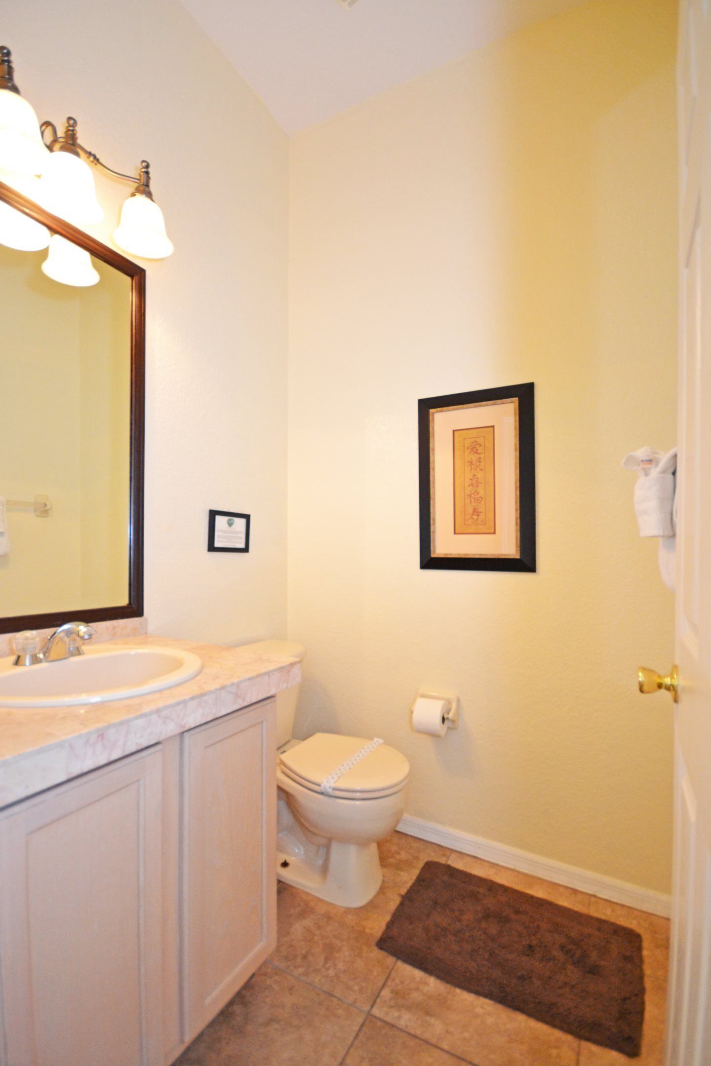 A bathroom with a sink, mirror, toilet, framed picture, and a towel rack.