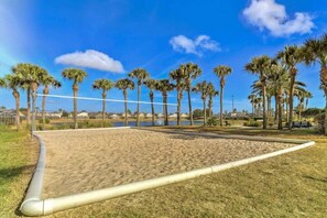 Play volleyball on the sandy court surrounded by palm trees and a clear view of the ocean.