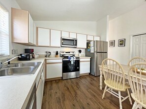 Efficient kitchen with microwave, stainless steel refrigerator, and dishwasher, plus a dining area with a wooden table and chairs.