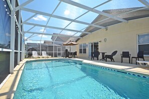 Ein überdachter Swimmingpool mit Liegestühlen und Tischen, einer Glasdecke und Blick auf den Himmel.