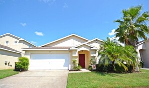 A single-story house with a garage and a front door, set amidst a well-manicured lawn and a palm tree.