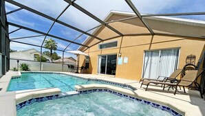 A swimming pool with a hot tub, surrounded by a covered patio with lounge chairs. - Beautifully updated three bedroom, two bath pool home with spa and games room! (Davenport)