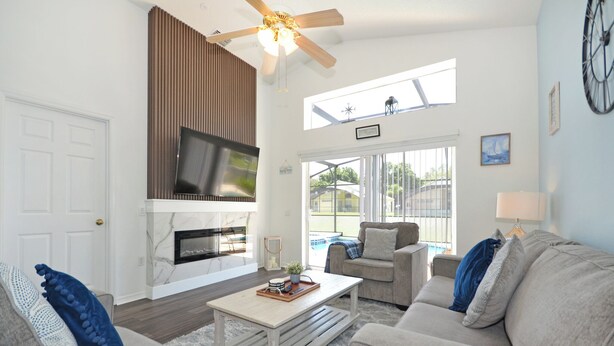 A spacious living room with a fireplace, a ceiling fan, and a large window offering a view of the outdoors. - Beautifully updated three bedroom, two bath pool home with spa and games room! (Davenport)