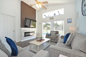 A spacious living room with a fireplace, a ceiling fan, and a large window offering a view of the outdoors. - Beautifully updated three bedroom, two bath pool home with spa and games room! (Davenport)