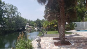 A riverside walkway with a statue, a pool, and lush greenery. - A PIECE OF PARADISE - MANATEE PLAYGROUND (Weeki Wachee)