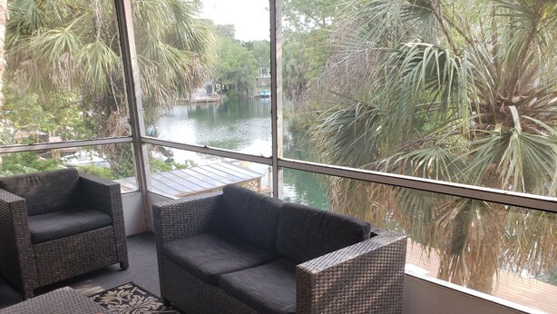 A room with wicker furniture, a view of a water body, and a patterned rug. - A PIECE OF PARADISE - MANATEE PLAYGROUND (Weeki Wachee)