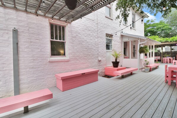 A deck with pink benches and planters, a pergola, and a white brick building with windows.