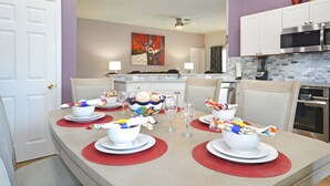 A dining area with a table set for four, surrounded by chairs, and a kitchen in the background. - Home from home! Updated - private pool & hot tub - gated resort (Clermont)