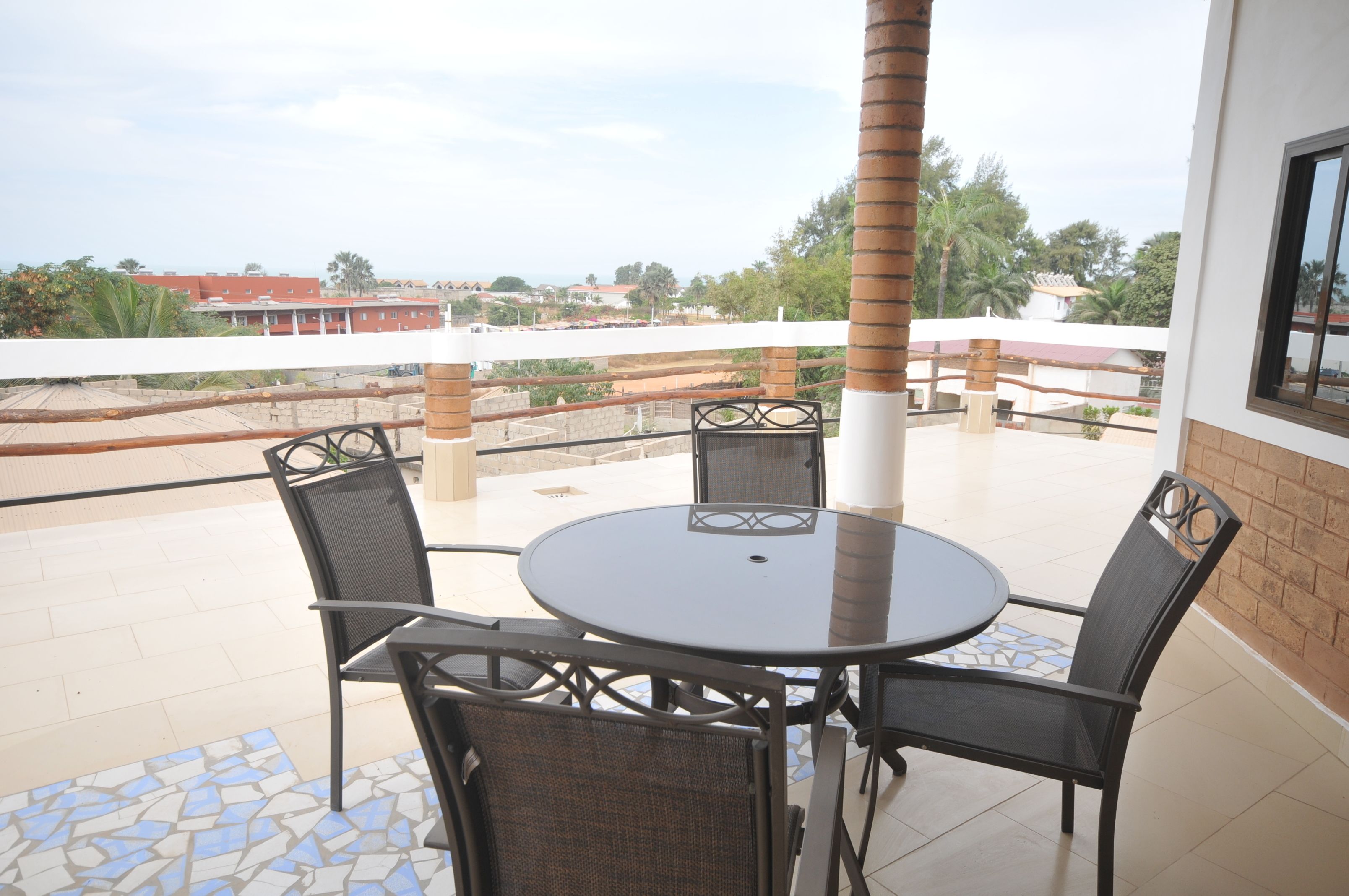 Een ronde tafel met vier stoelen op een balkon met een betegelde vloer en uitzicht op gebouwen en bomen.