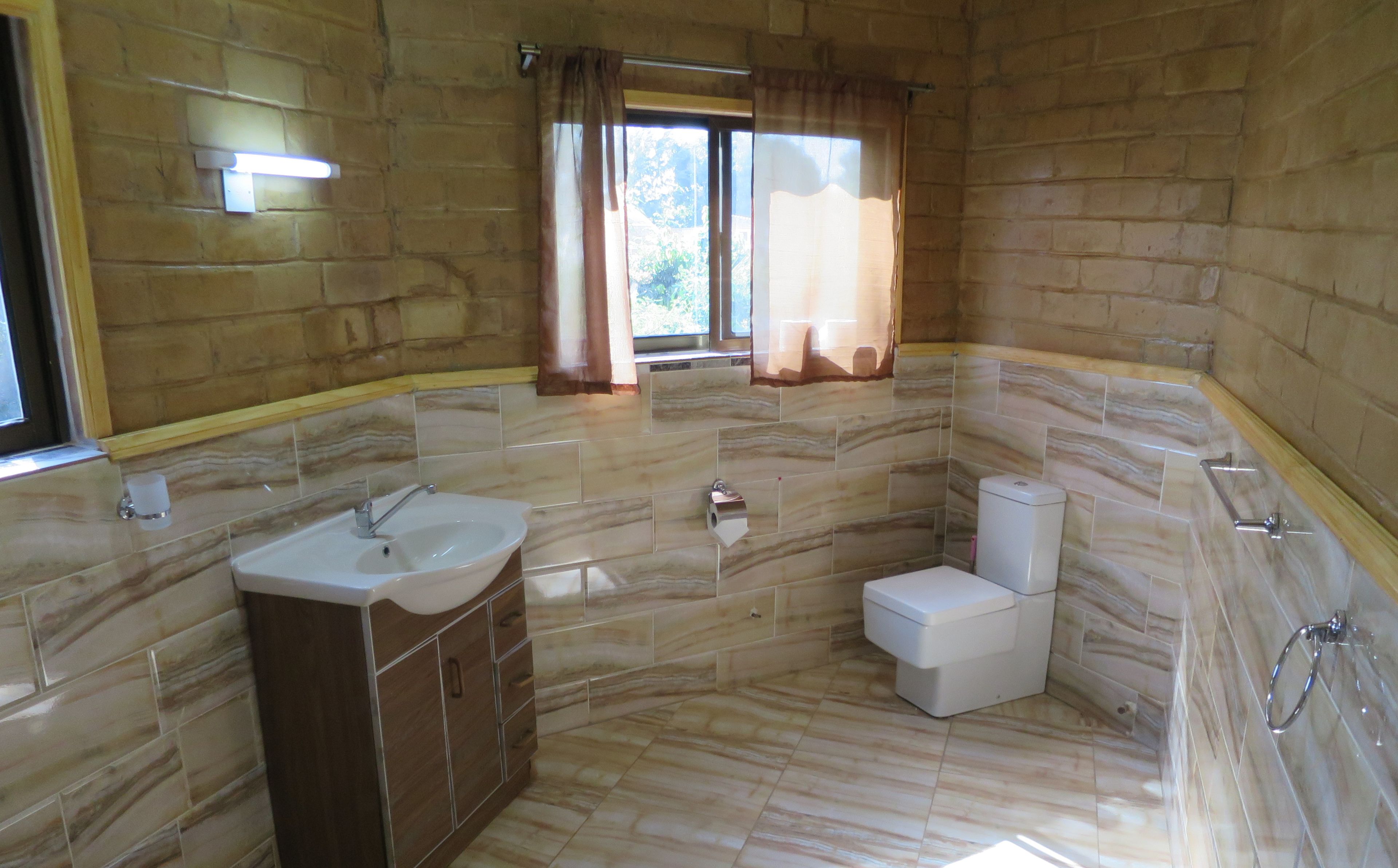 A bathroom with a marble sink, toilet, and shower area, featuring a window with curtains.
