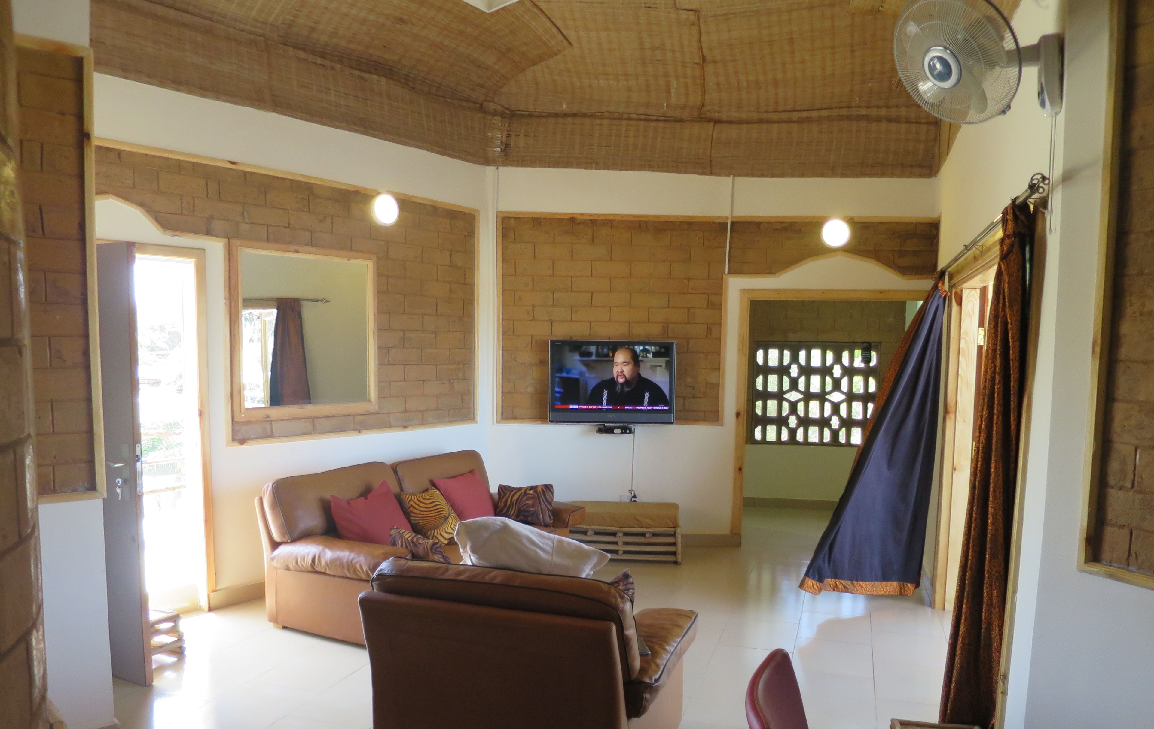 A living room with a brick wall, a television, a sofa, and a fan.