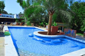 A swimming pool with a palm tree, a mural, and a building in the background.