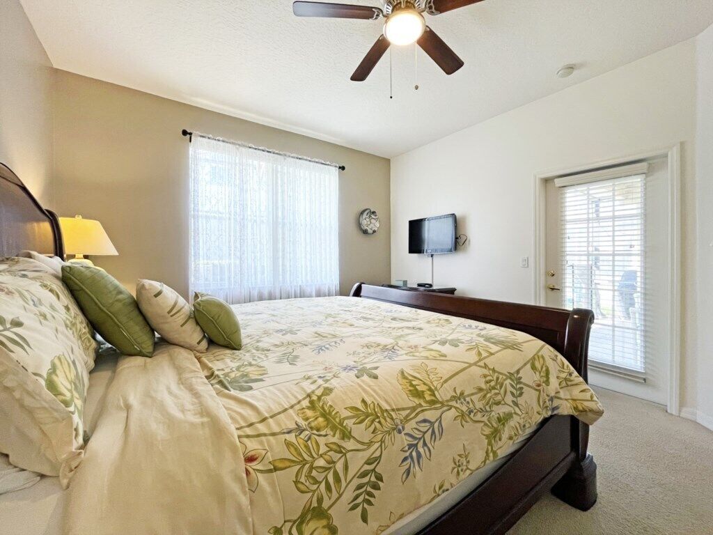 A bedroom with a bed, a ceiling fan, a TV, and a window.