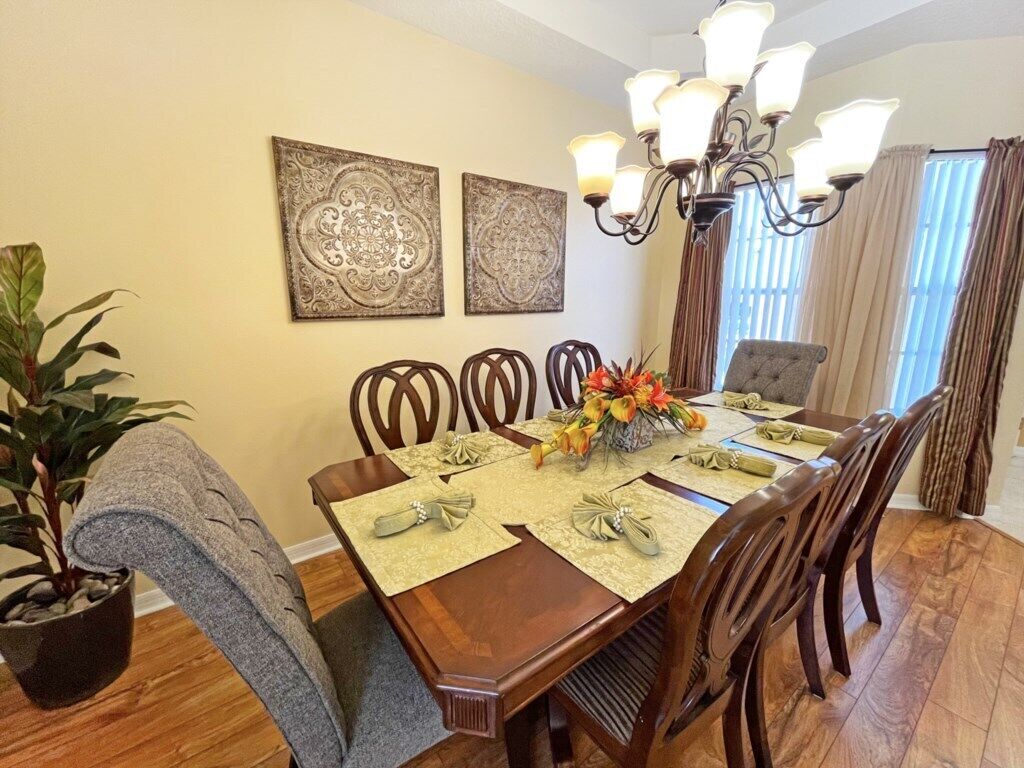 Een eetkamer met een houten tafel voor vier personen, omringd door stoelen. Boven de tafel hangen twee decoratieve wandpanelen.