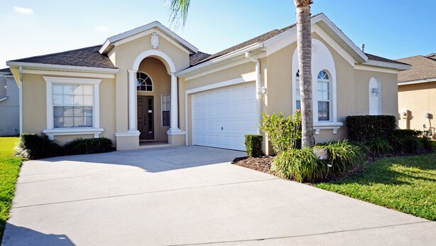 A single-story house with a garage, a front entrance with an archway, and a palm tree in the front yard. - Superior family vacation home (Haines City)