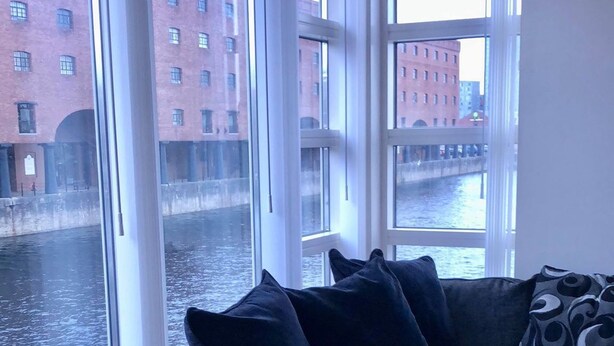 A room with a large window overlooking a canal, a dark blue sofa with cushions, and a patterned pillow.