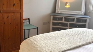 A bedroom with a large bed, a wooden wardrobe, a dresser with drawers, and a mirror on top.