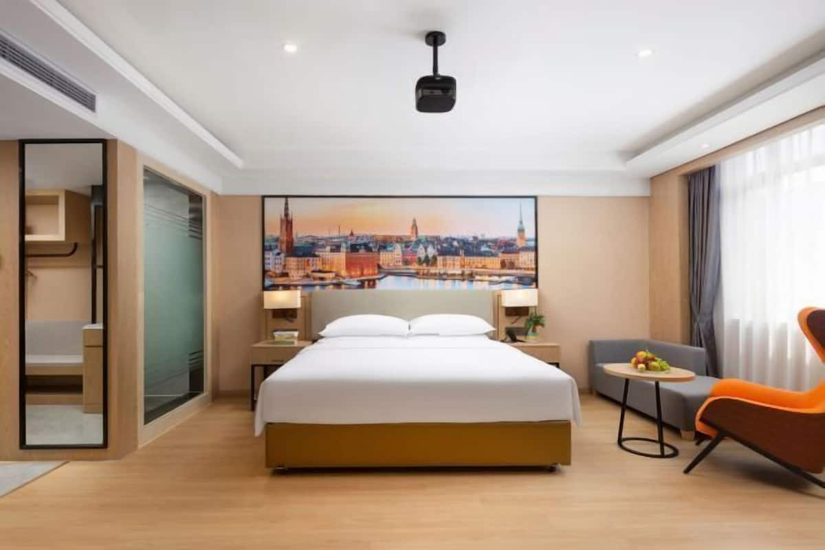 Une chambre d’hôtel avec un lit, un tableau représentant un paysage urbain, un bureau, une chaise et une fenêtre.