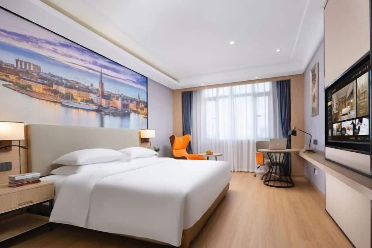 Une chambre d’hôtel équipée d’un lit, d’un bureau, d’une chaise, d’une télévision et d’une grande fenêtre avec des rideaux.