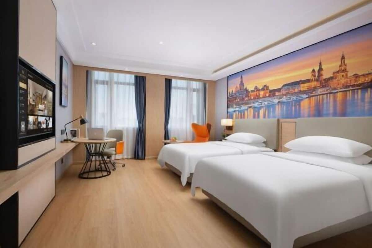 Une chambre d’hôtel avec deux lits, un bureau avec une chaise, une télévision et un tableau représentant un paysage urbain accroché au mur.