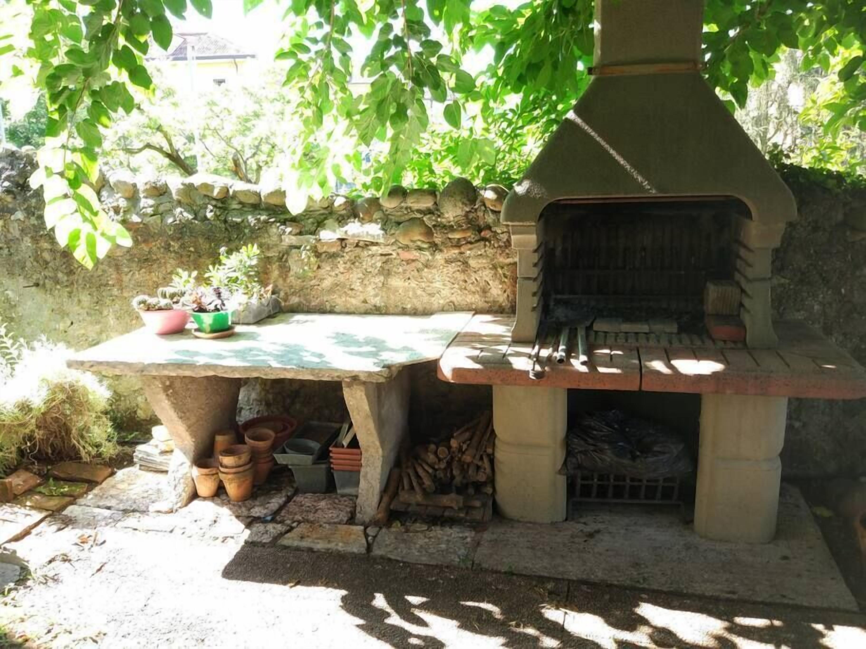 An outdoor stone oven with a rustic design, surrounded by potted plants and a stone wall.