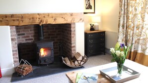 A cozy room with a fireplace, a wooden mantel, a table with a vase of flowers, and a framed picture on the wall.