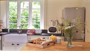 A kitchen with a window, a refrigerator, a microwave, and a wooden table with food items.
