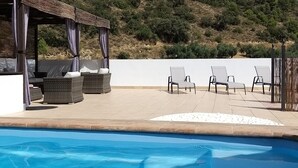 A poolside area with a covered seating area, lounge chairs, and a view of a hillside. - Casa Los Molinos with heated pool in the middle of nature (Montefrio)