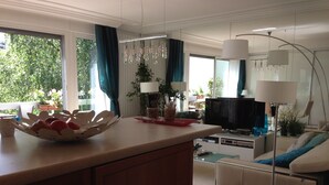 A modern living room with a sofa, a television, and a kitchen area with a fruit bowl. - Sweet Home Paris 12ème in lush greenery. Well located (Paris)
