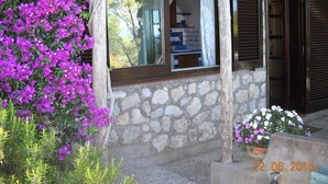 Ein Steingebäude mit Fenster und Fensterläden, umgeben von violettem Bougainvillea und einem Blumentopf mit weißen Blüten.