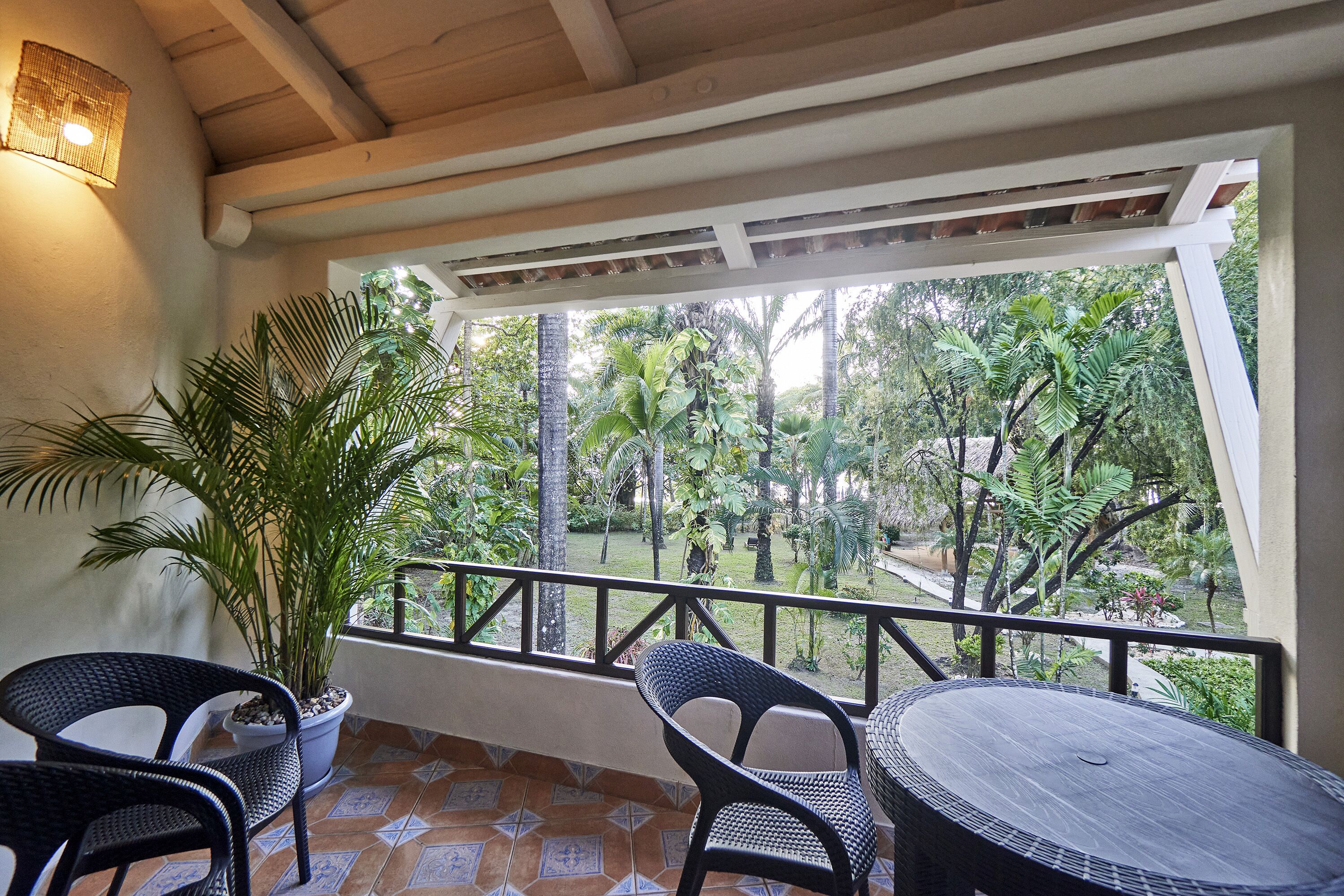 A covered outdoor area with a table and chairs, surrounded by potted plants and a view of a lush garden.