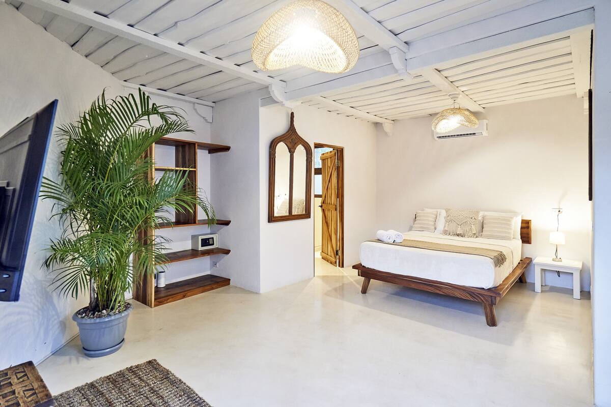A bedroom with a bed, bedside table, lamp, and a large potted plant.