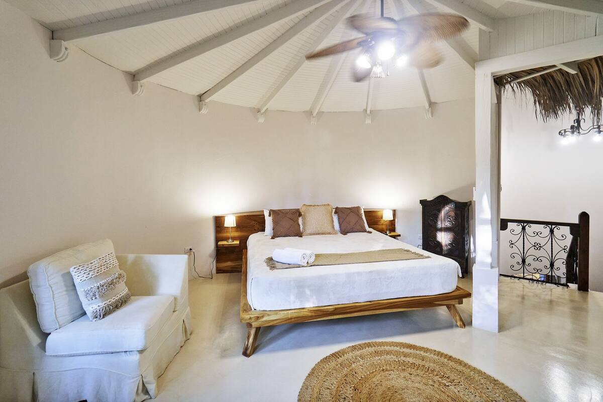 A bedroom with a bed, a nightstand, a chair, a ceiling fan, and a woven rug.