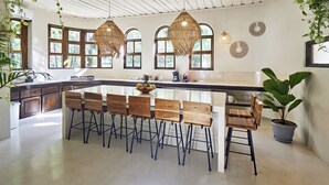 A modern kitchen with a large island, wooden chairs, hanging wicker lights, and large windows. - Paradise Beach Lodge (Cóbano)