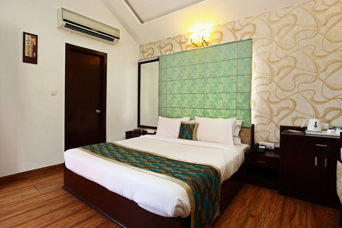 Habitación de hotel con una cama grande, una mesita de noche, un aparador, aire acondicionado y una lámpara fijada a la pared.