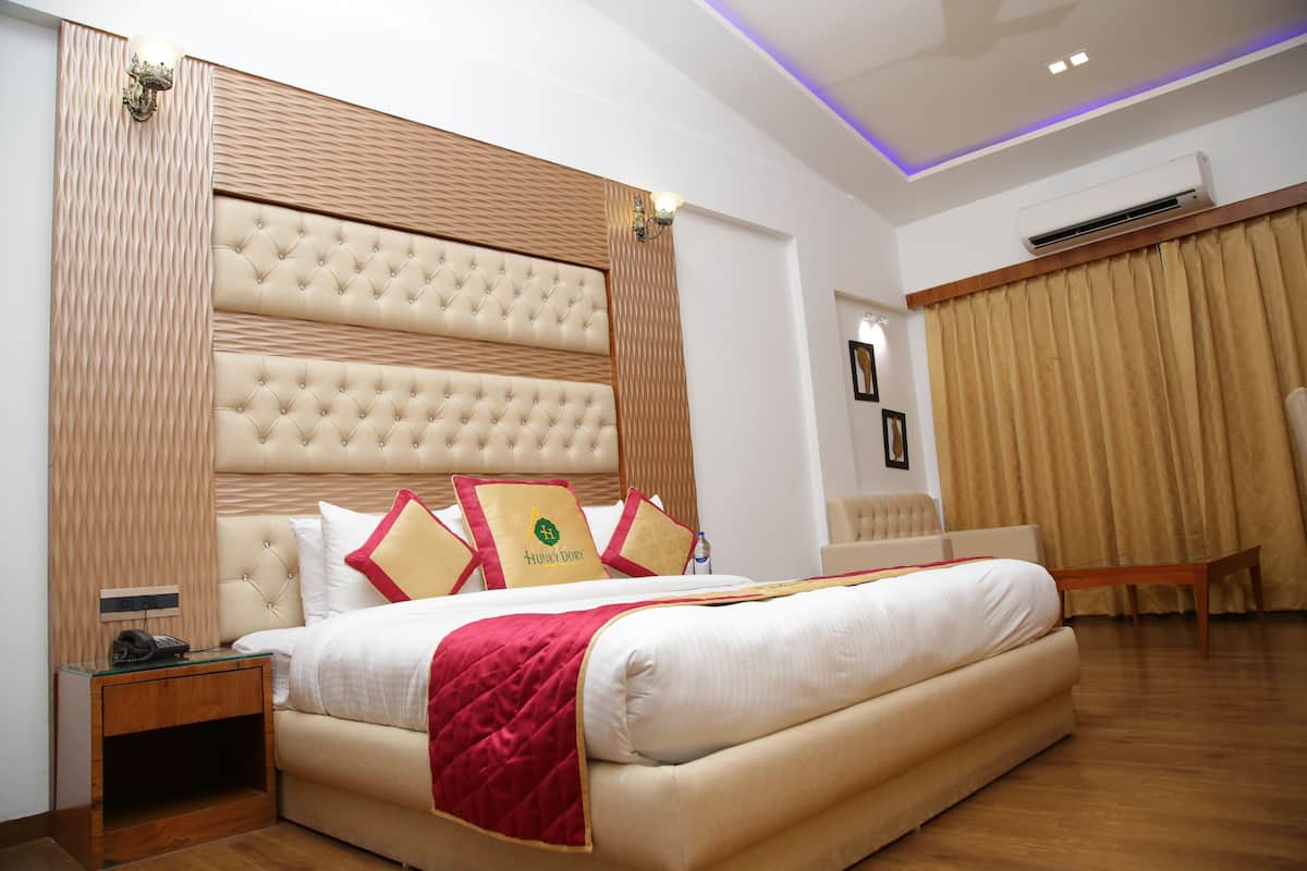 Habitación de hotel con una cama grande, cabecera de madera, mesita de noche y una silla.