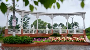 A pavilion with white columns and statues, surrounded by a flower bed with various flowers. - Hunky Dory Resort (Dhar Kalan)