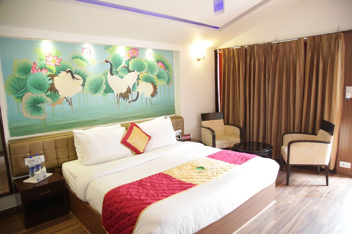 Una habitación de hotel con una cama grande, una mesita de noche, una silla, una mesa y un mural con pájaros y flores en la pared.