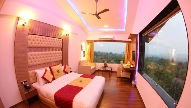 A modern hotel room with a large bed, a ceiling fan, a seating area with a view, and a large window. - Hunky Dory Resort (Dhar Kalan)