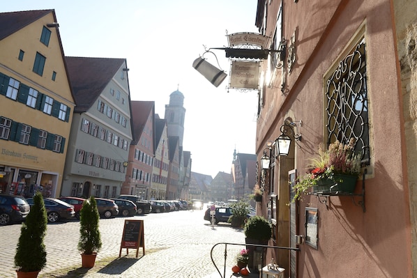 A cobblestone street lined with traditional European buildings, a parked car, and a sign for a hotel and restaurant. - Eisenkrug (Dinkelsbuehl)