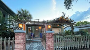 A house with a wooden picket fence, a brick entrance, and a porch with a decorative railing.