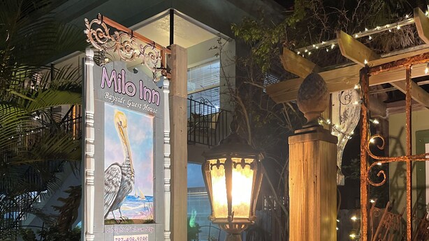A night-time view of a guesthouse with a sign advertising 'Milo Inn Bayside Guest House' and a contact number.