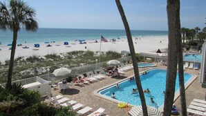 A pool area with lounge chairs and umbrellas, a beach with umbrellas and people, and a clear view of the ocean. - DIRECT BEACHFRONT - PENTHOUSE CORNER UNIT!!  Totally Renovated! (Indian Shores)