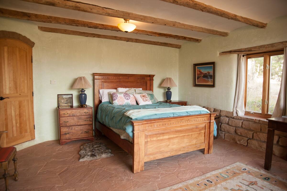 A bedroom with a wooden bed, stone walls, a stone fireplace, and a window with curtains.